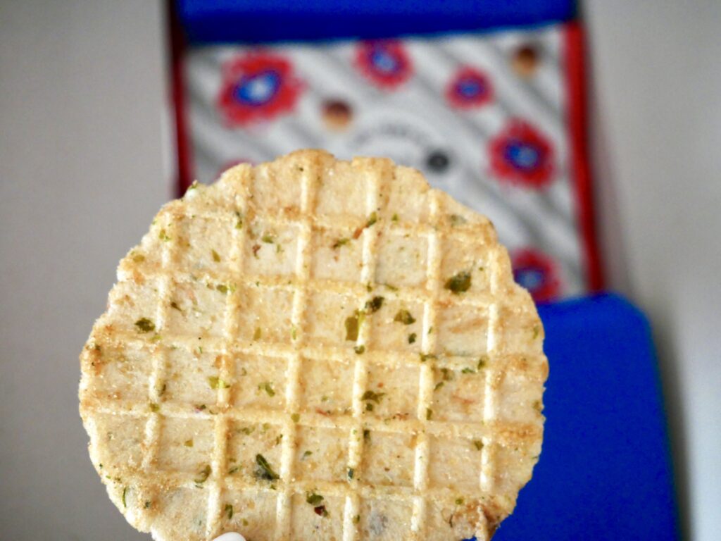 大阪万博限定「ミャクミャクたこ焼きせんべい」を手に取った写真。ソースの香りと青のりが香ばしい、薄焼きのせんべい。