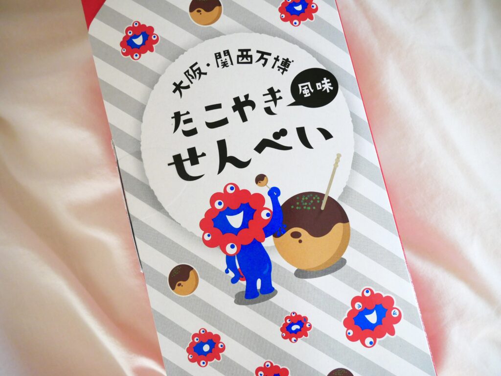 大阪・関西万博2025限定の「ミャクミャクたこ焼きせんべい」パッケージ。ミャクミャクとたこ焼きのイラストが描かれたデザインで、関西らしさが感じられる人気おみやげ。