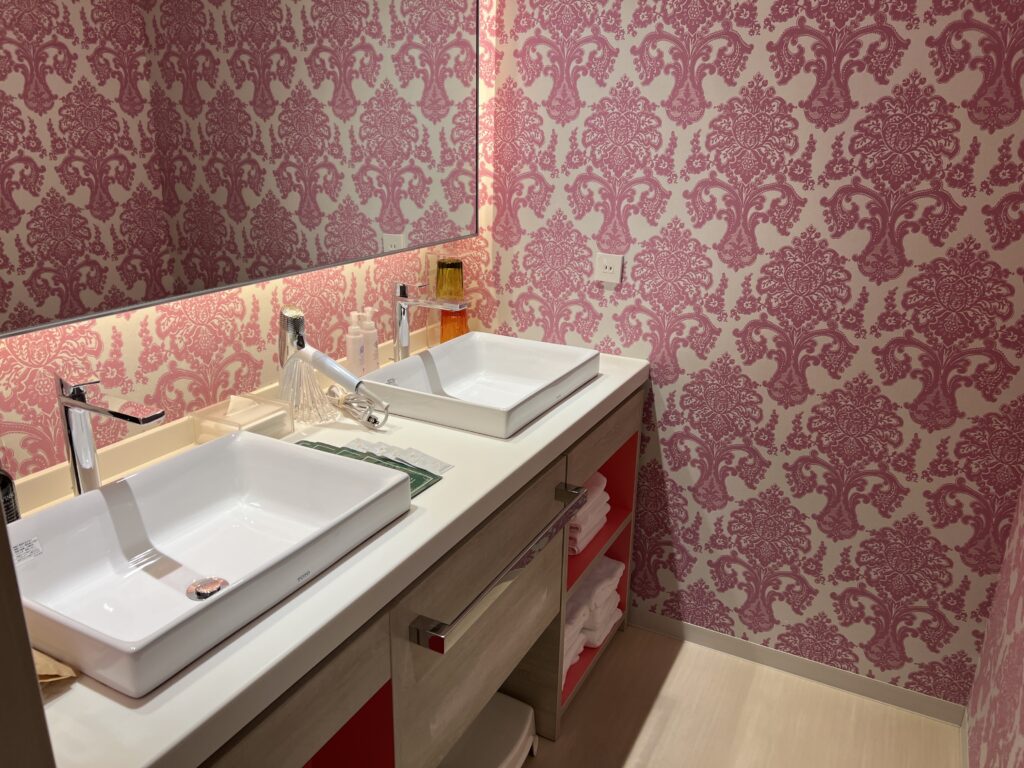 Bathroom at Hotel Universal Port Vita with pink wallpaper and two sinks, perfect for families.