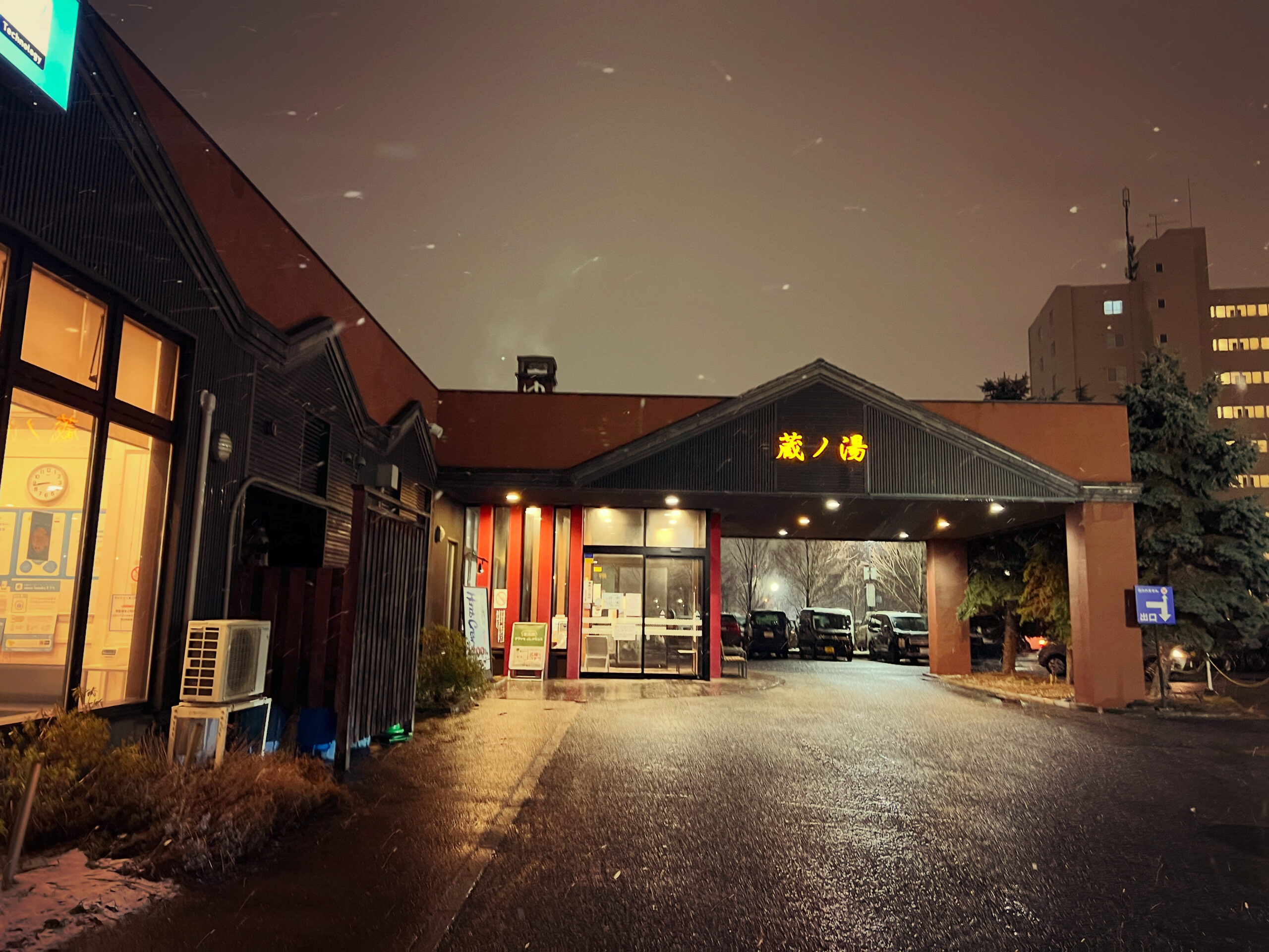 Night view of Kura-no-Yu, a popular local hot spring near Sapporo Station, with warm lights and light snowfall.