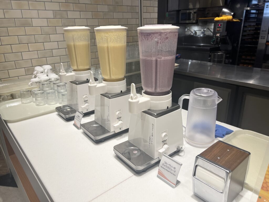 Three smoothie blenders filled with banana, yogurt, and blueberry flavors at the breakfast buffet.