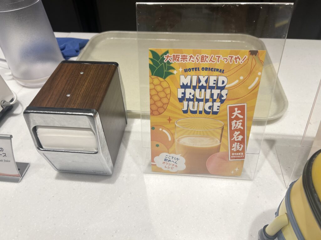 ホテルユニバーサルポートヴィータの朝食ビュッフェに設置された大阪名物ミックスジュースの案内ポップ。バナナや桃などのフルーツが描かれたデザイン。